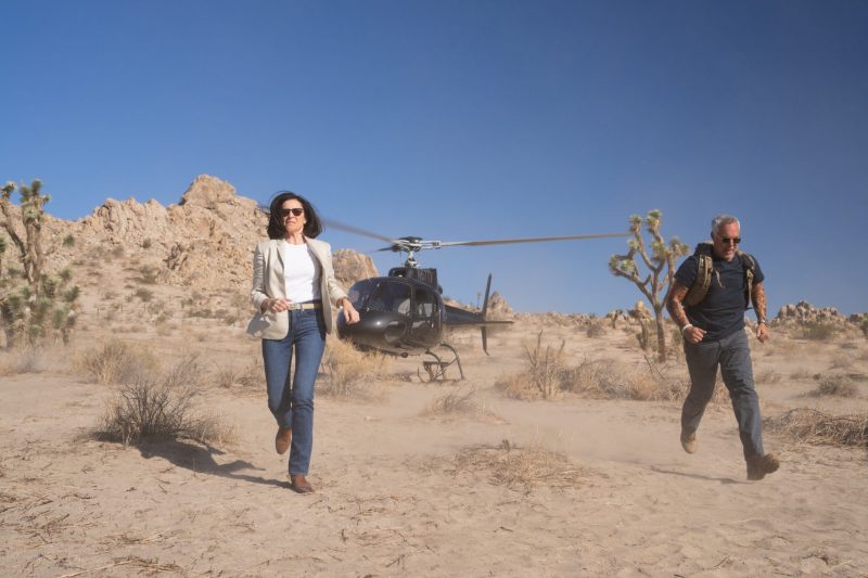 Bosch: Legacy characters Honey Chandler and Harry Bosch running in the desert with a helicopter landed behind them.