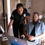 Bosch: Legacy characters, Officer Reina Vasquez (standing) and Mo Bassi (seated), look at a laptop screen.
