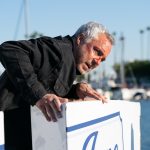 Bosch: Legacy character Harry Bosch leans against the edge of a boat with blood on his face and wearing a black jacket