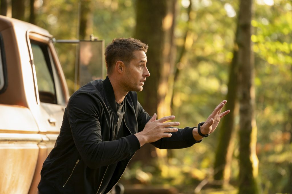 Justin as Colter Shaw in TRACKER in the woods with hands raised and wearing a black jacket
